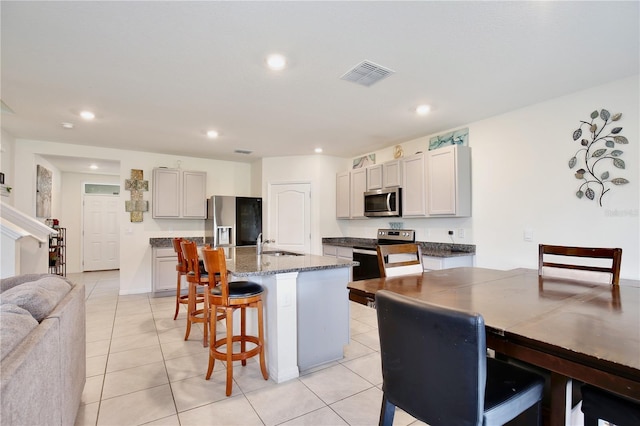 kitchen featuring a kitchen island with sink, a kitchen breakfast bar, sink, light tile patterned floors, and appliances with stainless steel finishes