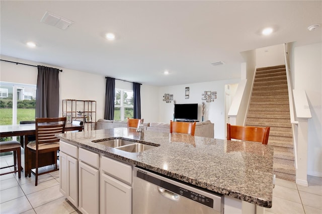 kitchen featuring sink, light tile patterned floors, dishwasher, white cabinetry, and an island with sink