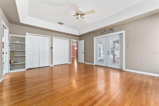 unfurnished bedroom featuring ceiling fan, french doors, light wood-type flooring, a tray ceiling, and access to outside