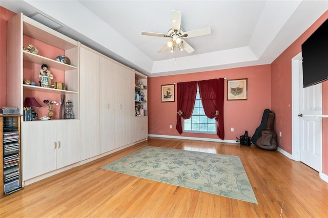 interior space featuring a tray ceiling, built in shelves, ceiling fan, and light hardwood / wood-style flooring