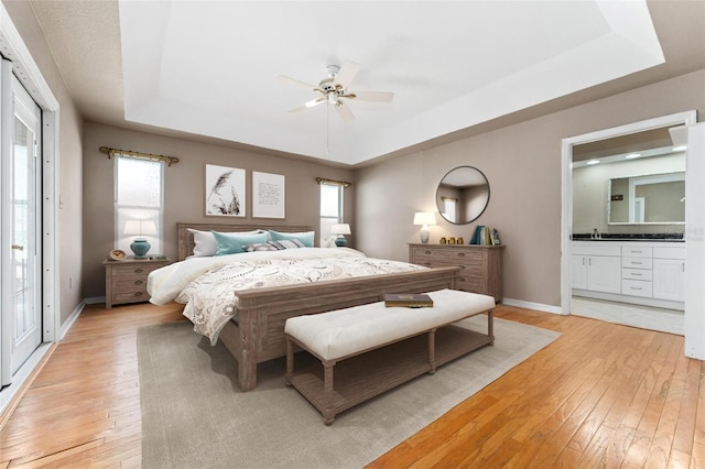 bedroom featuring ceiling fan, a raised ceiling, connected bathroom, and light hardwood / wood-style flooring