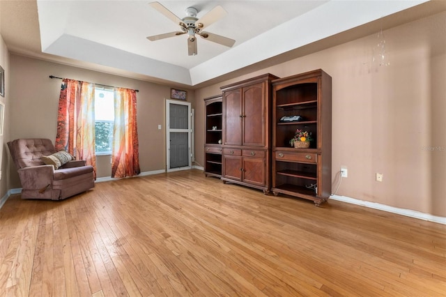 living area with ceiling fan, light hardwood / wood-style flooring, and a tray ceiling