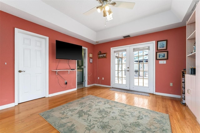 interior space featuring ceiling fan, light wood-type flooring, french doors, and a tray ceiling