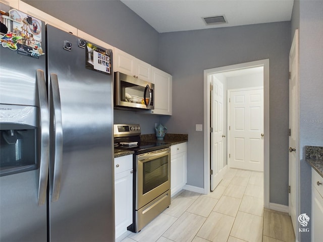 kitchen featuring white cabinets, appliances with stainless steel finishes, light tile patterned floors, and dark stone countertops