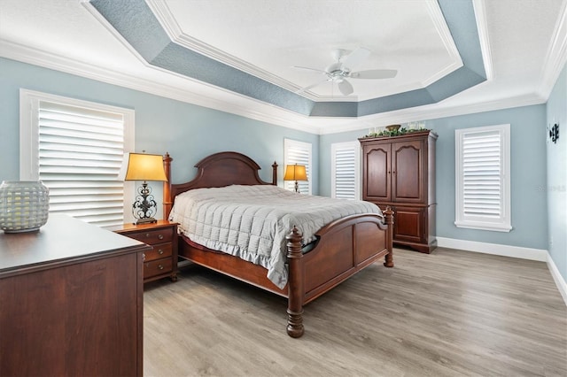 bedroom featuring light wood-type flooring, a raised ceiling, ceiling fan, and crown molding