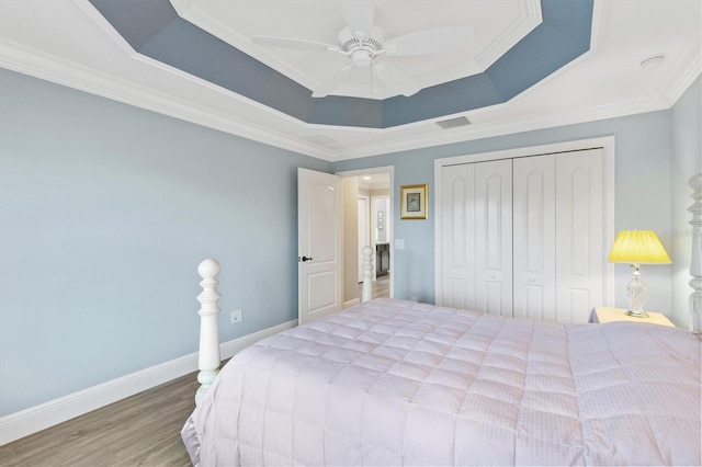 bedroom featuring ornamental molding, a tray ceiling, ceiling fan, hardwood / wood-style flooring, and a closet