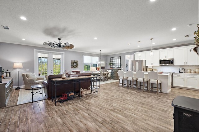 living room with a textured ceiling, light hardwood / wood-style floors, ceiling fan, and crown molding