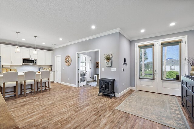 foyer with a textured ceiling, light wood-type flooring, crown molding, and french doors