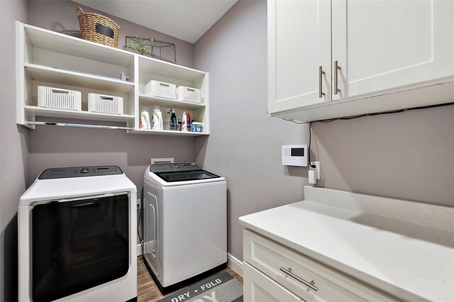 clothes washing area with washer and dryer, dark hardwood / wood-style flooring, and cabinets