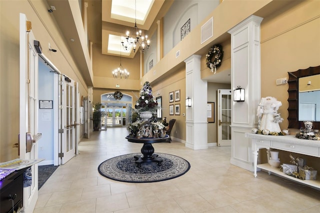 entrance foyer with french doors, a high ceiling, a notable chandelier, decorative columns, and light tile patterned floors