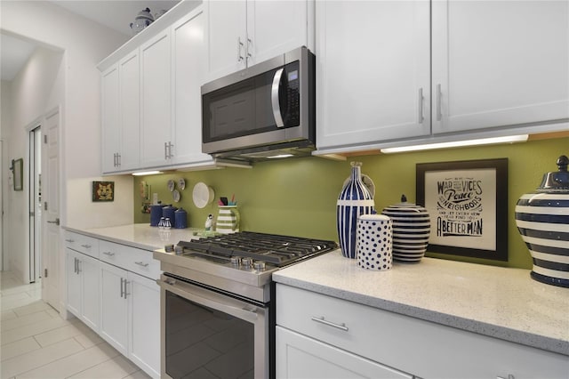 kitchen featuring white cabinets, appliances with stainless steel finishes, light tile patterned floors, and light stone countertops