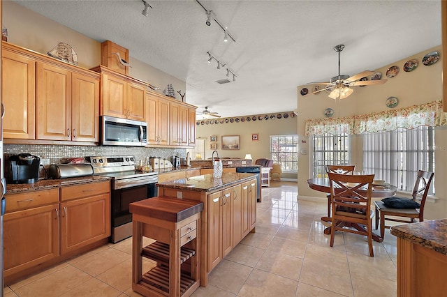 kitchen with backsplash, a textured ceiling, stainless steel appliances, a kitchen island, and light tile patterned flooring