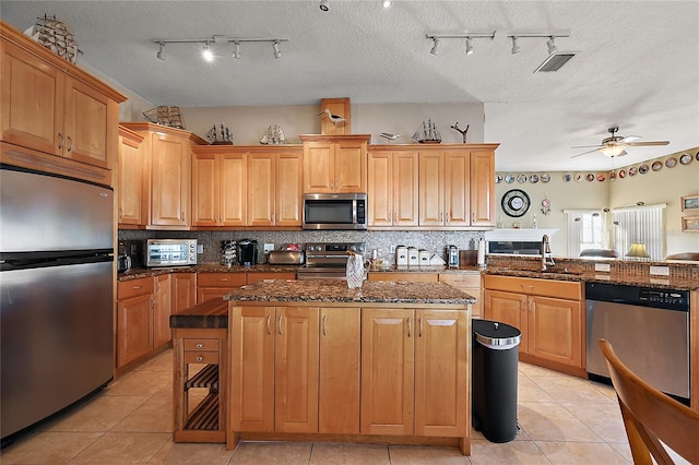 kitchen featuring a center island, sink, ceiling fan, a textured ceiling, and appliances with stainless steel finishes