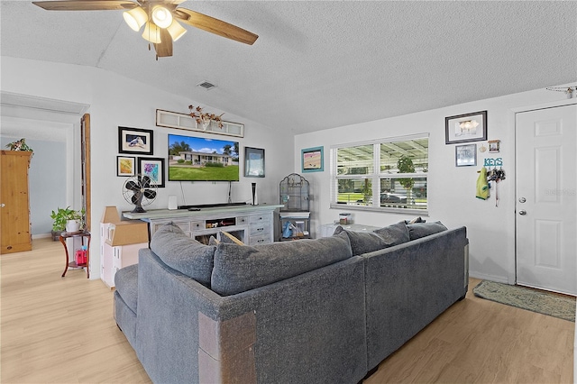 living room with a textured ceiling, light hardwood / wood-style flooring, vaulted ceiling, and ceiling fan