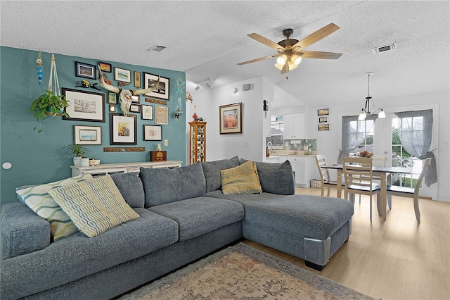 living room with a textured ceiling, light hardwood / wood-style flooring, ceiling fan with notable chandelier, and vaulted ceiling