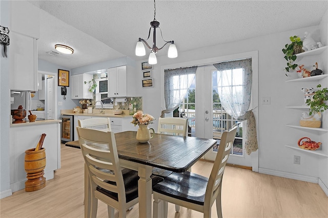 dining area with beverage cooler, light hardwood / wood-style floors, and a textured ceiling