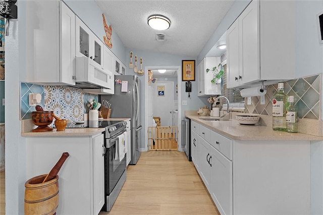 kitchen with appliances with stainless steel finishes, a textured ceiling, sink, light hardwood / wood-style floors, and white cabinetry