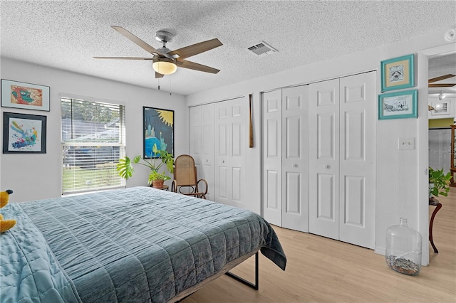 bedroom featuring multiple closets, ceiling fan, light hardwood / wood-style floors, and a textured ceiling