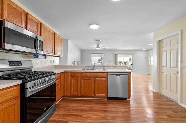 kitchen with ceiling fan, sink, kitchen peninsula, appliances with stainless steel finishes, and hardwood / wood-style flooring