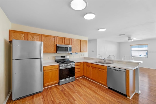 kitchen with sink, ceiling fan, appliances with stainless steel finishes, light hardwood / wood-style floors, and kitchen peninsula