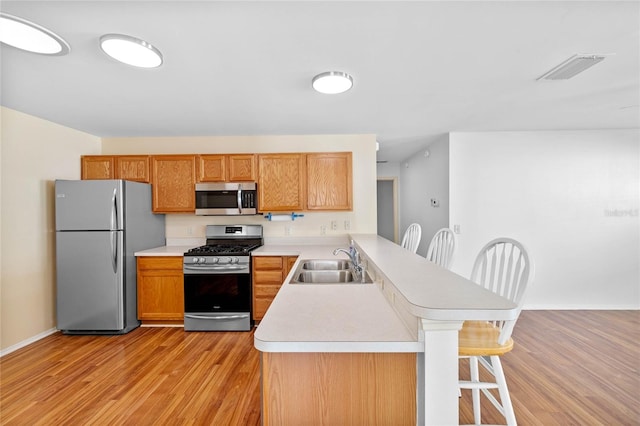 kitchen featuring a breakfast bar, sink, appliances with stainless steel finishes, light hardwood / wood-style floors, and kitchen peninsula