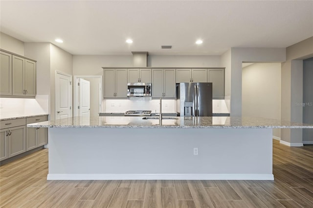 kitchen featuring light stone countertops, backsplash, a kitchen island with sink, and stainless steel appliances