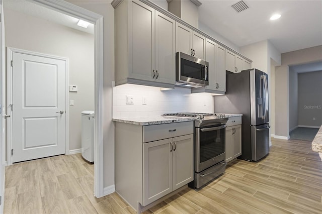 kitchen with appliances with stainless steel finishes, light wood-type flooring, light stone counters, and gray cabinetry