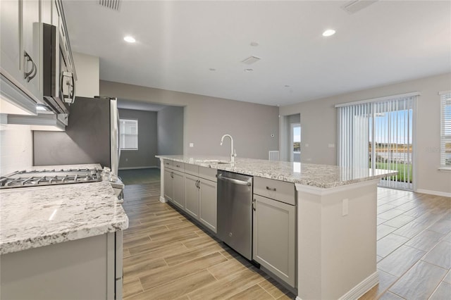 kitchen with a center island with sink, dishwasher, gray cabinets, and sink