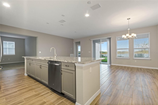 kitchen featuring dishwasher, sink, light stone counters, pendant lighting, and a center island with sink