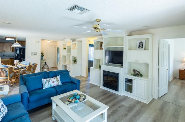 living room featuring ceiling fan, light hardwood / wood-style floors, and a textured ceiling