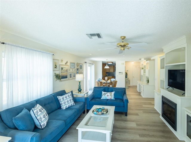 living room featuring ceiling fan, light wood-type flooring, and a textured ceiling