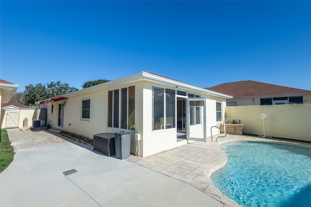 rear view of property with a sunroom, a storage unit, central AC, a fenced in pool, and a patio area