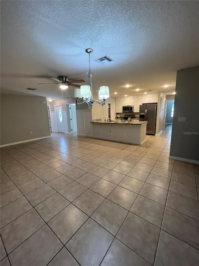 kitchen featuring hanging light fixtures, stainless steel appliances, kitchen peninsula, a textured ceiling, and white cabinets