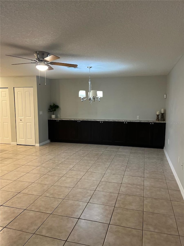 tiled empty room with ceiling fan with notable chandelier and a textured ceiling