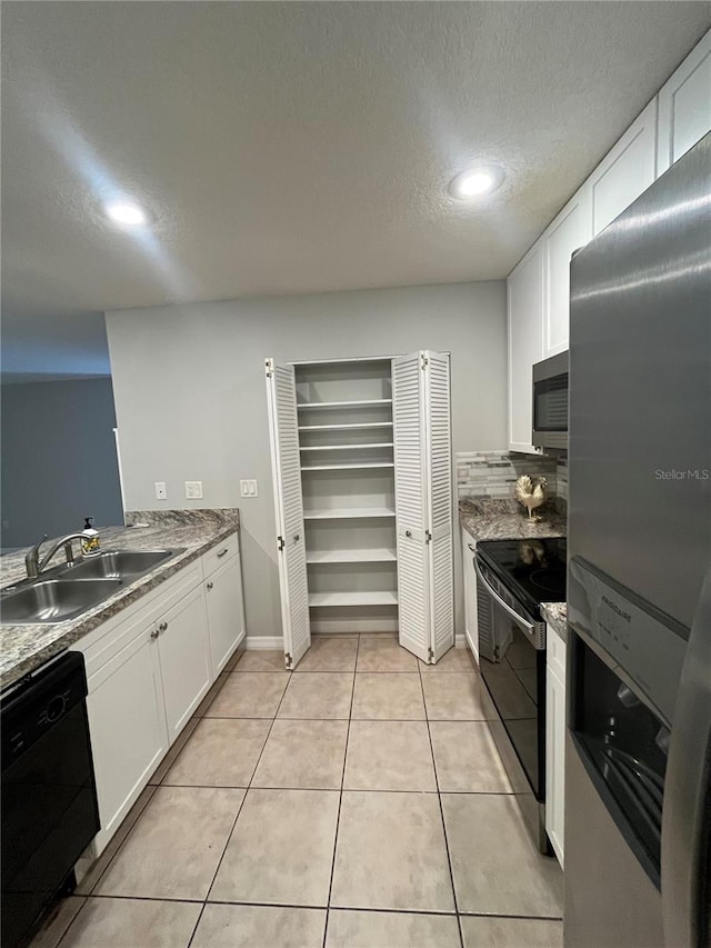 kitchen with appliances with stainless steel finishes, a textured ceiling, sink, light tile patterned floors, and white cabinetry