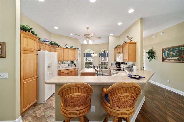 kitchen with kitchen peninsula, a kitchen breakfast bar, white appliances, a textured ceiling, and dark wood-type flooring