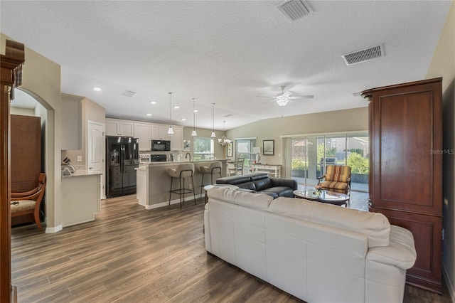 living room with ceiling fan, dark hardwood / wood-style flooring, a textured ceiling, and vaulted ceiling