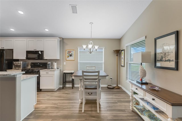 kitchen with light hardwood / wood-style flooring, a notable chandelier, pendant lighting, white cabinets, and black appliances