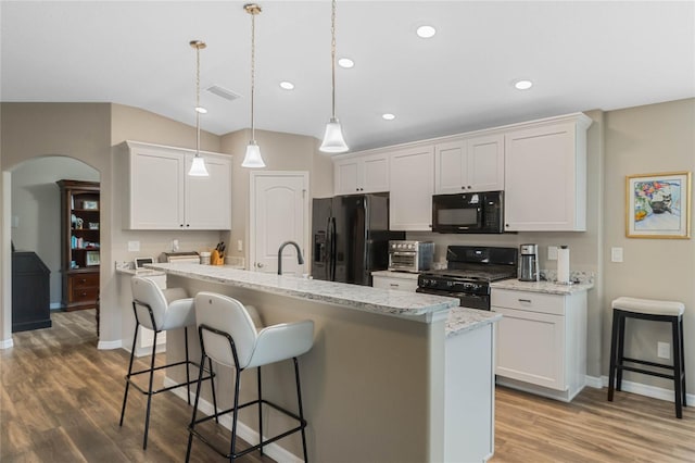 kitchen featuring black appliances, hardwood / wood-style floors, white cabinetry, hanging light fixtures, and a breakfast bar area