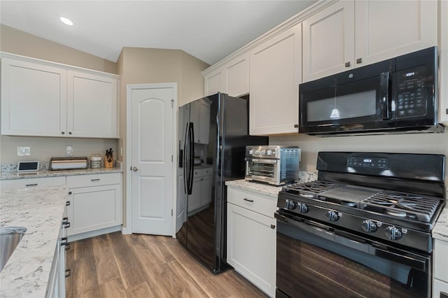 kitchen with light stone counters, hardwood / wood-style floors, white cabinets, and black appliances