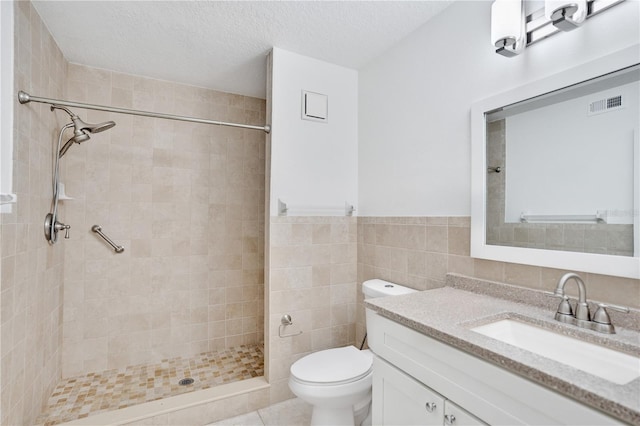 bathroom with vanity, a textured ceiling, tiled shower, tile walls, and toilet