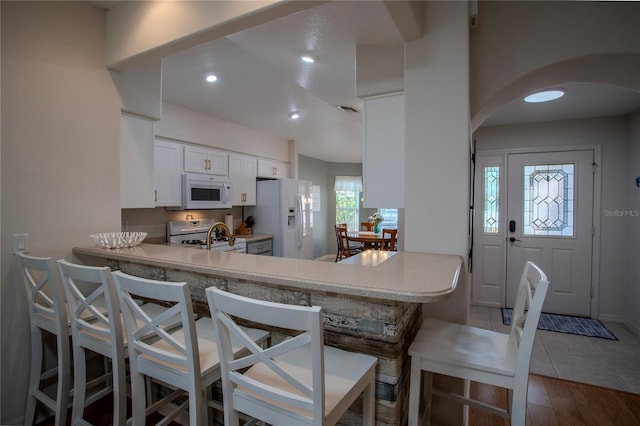 kitchen featuring a breakfast bar, white appliances, white cabinets, and kitchen peninsula