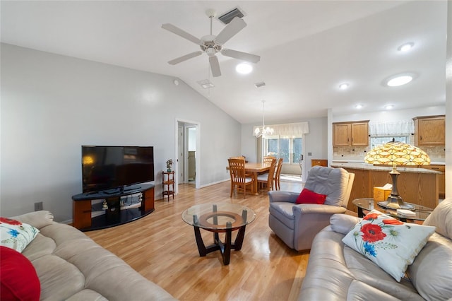 living room with ceiling fan with notable chandelier, lofted ceiling, and light hardwood / wood-style flooring