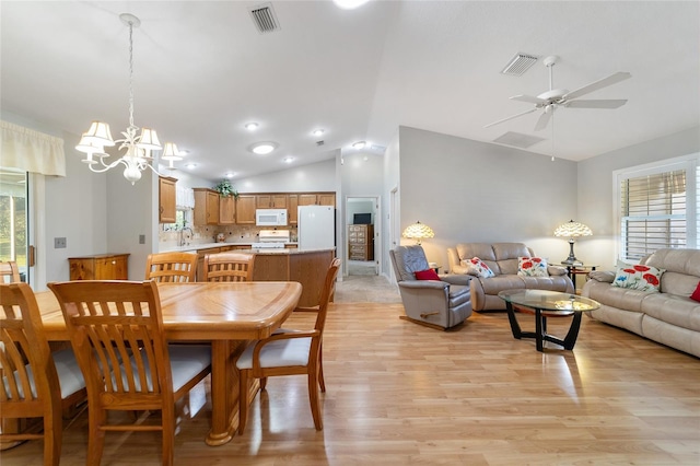 dining space with ceiling fan with notable chandelier, lofted ceiling, sink, and light hardwood / wood-style flooring