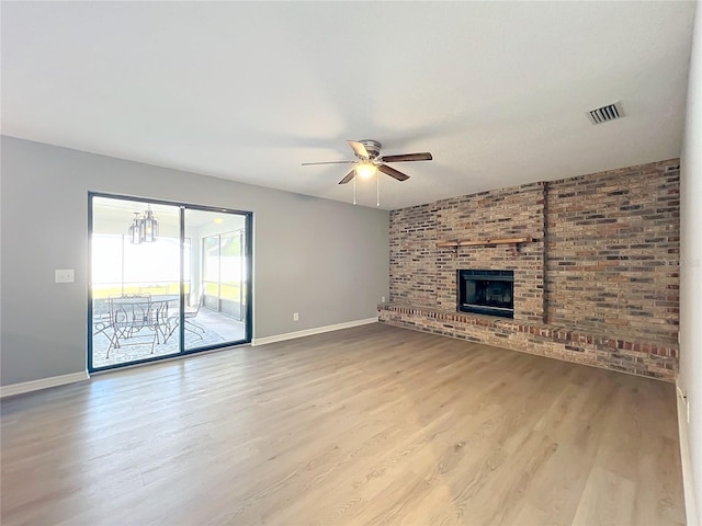 unfurnished living room featuring ceiling fan with notable chandelier, light wood-type flooring, a brick fireplace, and brick wall