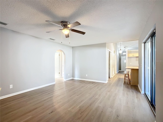 spare room with ceiling fan, a healthy amount of sunlight, a textured ceiling, and light wood-type flooring