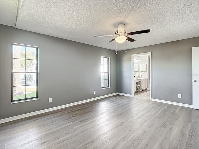 unfurnished bedroom featuring ensuite bathroom, ceiling fan, a textured ceiling, and light hardwood / wood-style flooring