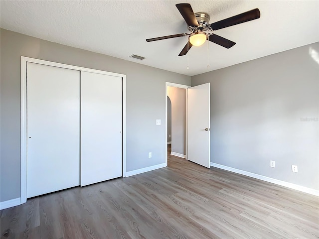 unfurnished bedroom featuring a closet, ceiling fan, light hardwood / wood-style flooring, and a textured ceiling