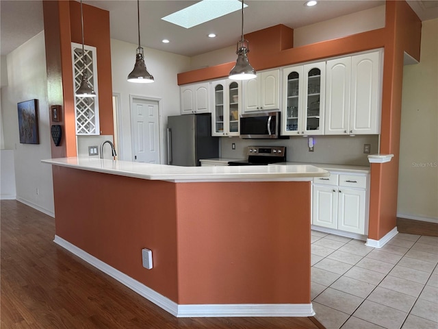 kitchen featuring a skylight, stainless steel appliances, sink, light tile patterned floors, and white cabinets