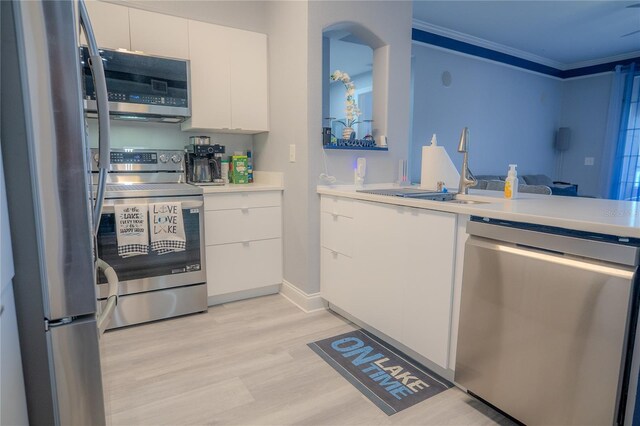 3406 Soho St Unit 102, Orlando, FL 32835 - kitchen featuring appliances with stainless steel finishes, white cabinets, light countertops, crown molding, and light wood-style floors